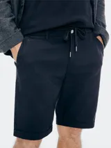 Bermuda de gabardina color beige con cintura elástica y cordón ajustable. Presenta bolsillos laterales y ruedo con dobladillo.