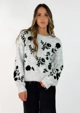 Sweater de tejido suave en color gris claro, con diseño de flores bordadas en color negro. Presenta cuello redondo, mangas largas y corte holgado.
