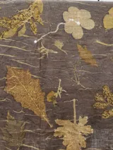 Mantel rectangular de lino color marrón con estampado de hojas y flores en tonos dorados y blancos.