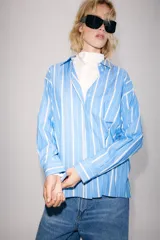 Camisa ZW Collection de algodón, con diseño a rayas verticales celestes y blancas, cuello solapa, manga larga y bolsillo de parche en el pecho con cierre frontal de botones ocultos.