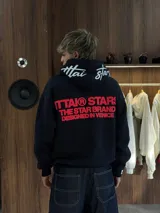Hoodie negro de corte oversize con capucha, confeccionado en algodón. Presenta un estampado gráfico en color rojo en la espalda con la leyenda 'ITTAI STARS THE STAR BRAND DESIGNED IN VENICE' y un detalle bordado en blanco en la parte posterior de la capucha.