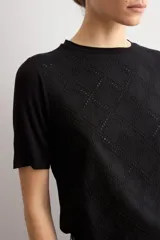 Remera negra de manga corta con panel frontal de tela broderie con diseño geométrico de rombos y espalda lisa.
