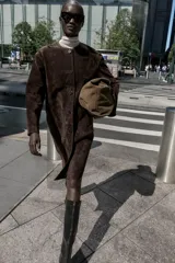 Abrigo marrón de gamuza con cuello redondo, manga larga, bolsillos delanteros y cierre frontal con botones.