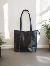 Bolso tote negro con textura croco, doble asa de hombro y detalle de trenzado en los laterales.