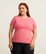 Blusa rosada de manga corta con cuello redondo decorado con una aplicación de perlas artificiales y strass a modo de collar.