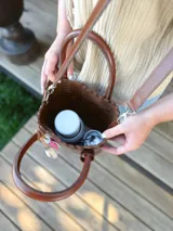 Bolso matera de cuero color marrón con doble asa de mano y correa larga desmontable. Incluye accesorio decorativo de borlas rosas y blancas.