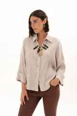 Camisa de textura plisada en color beige, con cuello clásico, cierre frontal de botones y mangas tres cuartos con puños vueltos.