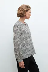 Blusa beige con estampado de lunares negros, cuello en V y mangas largas.