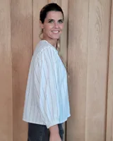 Camisa de manga larga con diseño de rayas verticales y bordados sutiles. Presenta cuello redondo, cierre frontal con botones y mangas abullonadas con volados en los hombros.