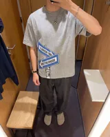 Remera de corte oversize color gris con efecto stone wash, con estampa frontal de carteles de señalización vial con la inscripción 'KABOA IND' y 'BROTHERHOOD'.