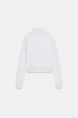 Chaqueta de felpa negra con cuello solapa, manga larga con puño, bolsillos de plastrón en el delantero y cierre frontal con cremallera.