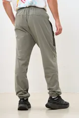 Pantalón deportivo gris con paneles laterales negros, cintura elástica y puños ajustados.