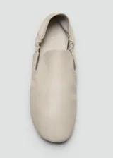 Zapatos tipo ballerinas planas de piel ovina en color blanco, con punta redonda, diseño sin cordones y detalle de fruncido elástico en el talón.