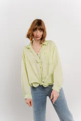 Camisa color verde claro con cuello camisero, botones frontales, bolsillo en el pecho y detalle de encaje en el escote. Se ata en la parte inferior delantera.