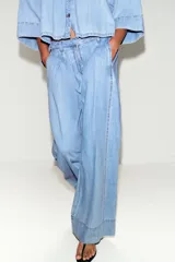 Jeans de tiro medio con corte wide leg y pinzas delanteras. Presenta bolsillos frontales, bolsillos de plastrón en la parte trasera, cierre frontal con cremallera, botón interior y ganchos metálicos.