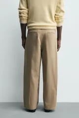 Pantalón chino de corte wide fit confeccionado en tejido de algodón. Presenta pliegues frontales, bolsillos laterales y bolsillos traseros de vivo, con cierre frontal de cremallera y botón.