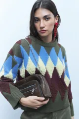 Bandolera de cuero vegano color marrón oscuro, con diseño rectangular y doble cierre frontal con tiradores metálicos. Incluye correa ajustable de cuero vegano y cadena metálica removible.