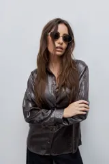 Camisa blanca de calce relajado con acabado satinado y brillo sutil, cuello clásico, cierre frontal con botones y mangas largas con puños.