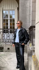 Campera de cuero sintético color negro, con cuello camisero, cierre frontal y costuras visibles en contraste. Presenta un diseño holgado con puños elásticos.