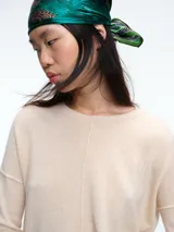 Sweater de tejido de punto color beige, con cuello redondo, manga larga y costura central vertical. Presenta un diseño con aberturas laterales en el ruedo y terminaciones acanaladas en puños y cuello.