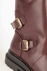 Bota corta negra de cuero sintético con caña asimétrica y dos hebillas metálicas.