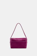 Mini bolso de mano confeccionado en piel de gamuza color fucsia. Presenta un diseño estructurado con asa corta, cierre principal mediante cremallera y solapa, y bolsillos exteriores en la parte frontal y trasera.