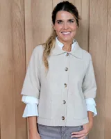 Cardigan de lana lambswool color beige, con cuello tipo polo, cierre frontal de botones y mangas cortas con terminación en puño tejido. Presenta bolsillos frontales aplicados.