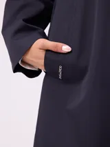 Gabardina de corte clásico en color azul marino, con cierre frontal de botones, cuello camisero y bolsillos laterales. Presenta un diseño minimalista con un pequeño bordado en el pecho.