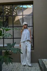 Pantalón de corte amplio y tiro alto, confeccionado en tela liviana de color blanco, con cintura elástica y cordón ajustable.