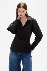Camisa negra de algodón con diseño cruzado y anudado lateral, cuello camisero y mangas largas con puños abotonados.