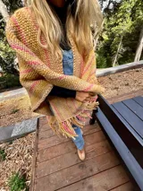 Ruana artesanal color crudo con rayas horizontales color ladrillo y flecos.