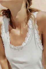 Musculosa de algodón color negro, con escote redondo y tiras anchas. Presenta detalles de encaje negro en los bordes y aplicación de perlas pequeñas alrededor del escote y los hombros.