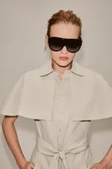 Vestido camisero midi de algodón con diseño de capa, cuello solapa, manga corta tipo capa y trabillas en los hombros. Presenta cierre frontal con botones, bolsillos delanteros y cinturón ajustable del mismo tejido con lazada. El bajo tiene un acabado en línea evasé.