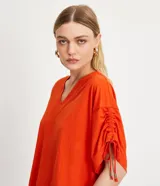 Blusa amplia color naranja, con escote en pico y mangas cortas con detalle de lazo fruncido.
