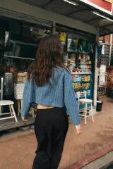 Chaqueta corta de cuello subido y manga larga, con diseño de cuadros en tonos azules. Presenta cierre frontal cruzado con botones oscuros y bolsillos de vivo en el delantero.