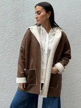 Tapado de eco cuero gamuzado color marrón con interior y bordes de corderito sintético color crema. Presenta diseño con capucha, bolsillos frontales y corte relajado.
