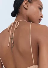 Vestido midi color beige, con diseño recto y escote halter con cierre de lazo en la espalda. El tejido principal es de lentejuelas.
