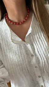 Collar corto de cuentas rojas con líneas horizontales blancas y cadena plateada para regular el largo.