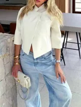 Chaqueta cropped de diseño estructurado en color crema, con cuello alto, cierre frontal cruzado con botones y mangas 3/4. Presenta un bolsillo decorativo en el frente y un corte asimétrico.