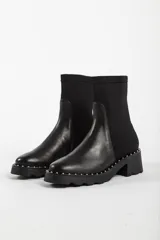 Bota de caña media color negro, con diseño tipo chelsea, suela track con detalle de tachas metálicas en el borde y elástico lateral.