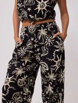 Pantalon de corte recto y holgado, confeccionado en algodón estampado con motivos playeros como palmeras, soles y caracoles en color crema sobre fondo negro. Posee cintura elástica.