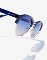 Gafas de sol Hawkers unisex, con montura azul y lentes degradadas de azul a rosa.