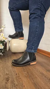 Botinetas de cuero negro estilo Chelsea, con paneles laterales elásticos, detalle de textura reptil en la parte trasera, costuras visibles en contraste y taco bajo de madera.