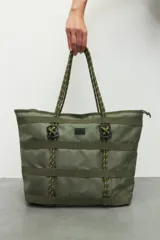 Bolso tipo tote color verde militar con múltiples correas horizontales y verticales. Tiene doble asa de soga trenzada y cierre superior con cremallera.