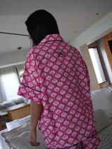 Pijama de dos piezas, compuesto por una camisa de manga corta con cuello solapa y botones frontales, y un short a juego. El conjunto es de color azul claro con un estampado repetitivo de pequeños motivos florales en color rosado/rojo, y ribetes de color rojo en los bordes de la camisa y el short.