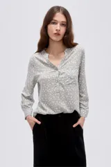 Blusa de viscosa con estampado de flores pequeñas en tonos grises y blancos, cuello en V con abotonadura parcial y bolsillo ojal en el pecho.