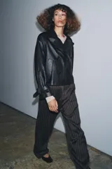 Cazadora corta de piel 100% negra, con cuello solapa de muescas, cierre frontal cruzado de doble botonadura, mangas largas ajustables con hebillas y bolsillos delanteros.