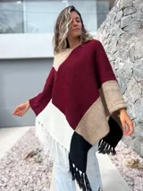 Poncho tejido de punto con diseño de bloques de color en tonos bordó, beige, blanco y negro, con terminación de flecos en el ruedo.