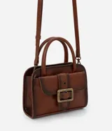 Cartera pequeña de mano con diseño estructurado, confeccionada en poliuretano color marrón con acabado envejecido. Cuenta con tapa frontal decorada con una hebilla metálica, cierre principal con cremallera, asa de mano rígida y correa larga ajustable y desmontable.