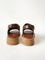 Sandalias de cuero color chocolate con suela track y taco bajo cuadrado. Poseen capellada cerrada con aberturas laterales y tira ajustable en el talón con hebilla metálica.